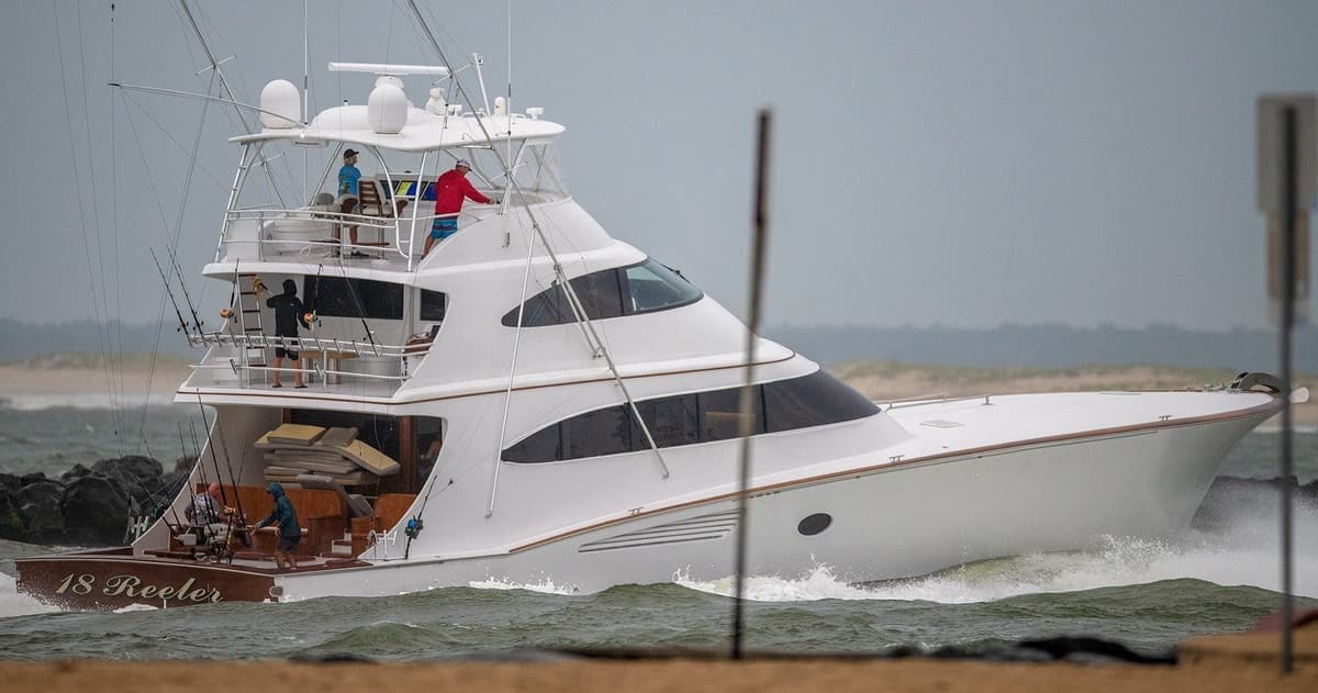 Sportfishing yacht cutting through waves with several people on deck against a cloudy backdrop