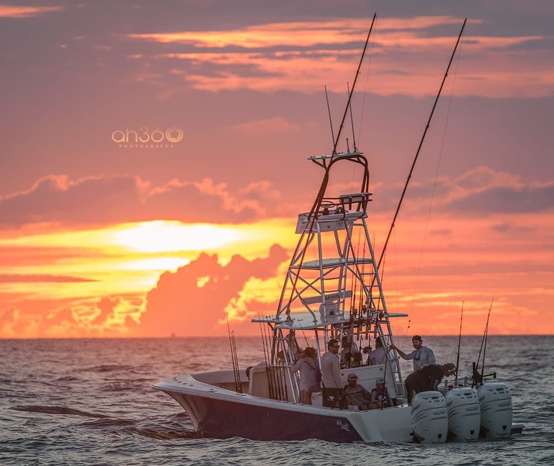 Sportfishing boat with multiple anglers set against a stunning ocean sunset