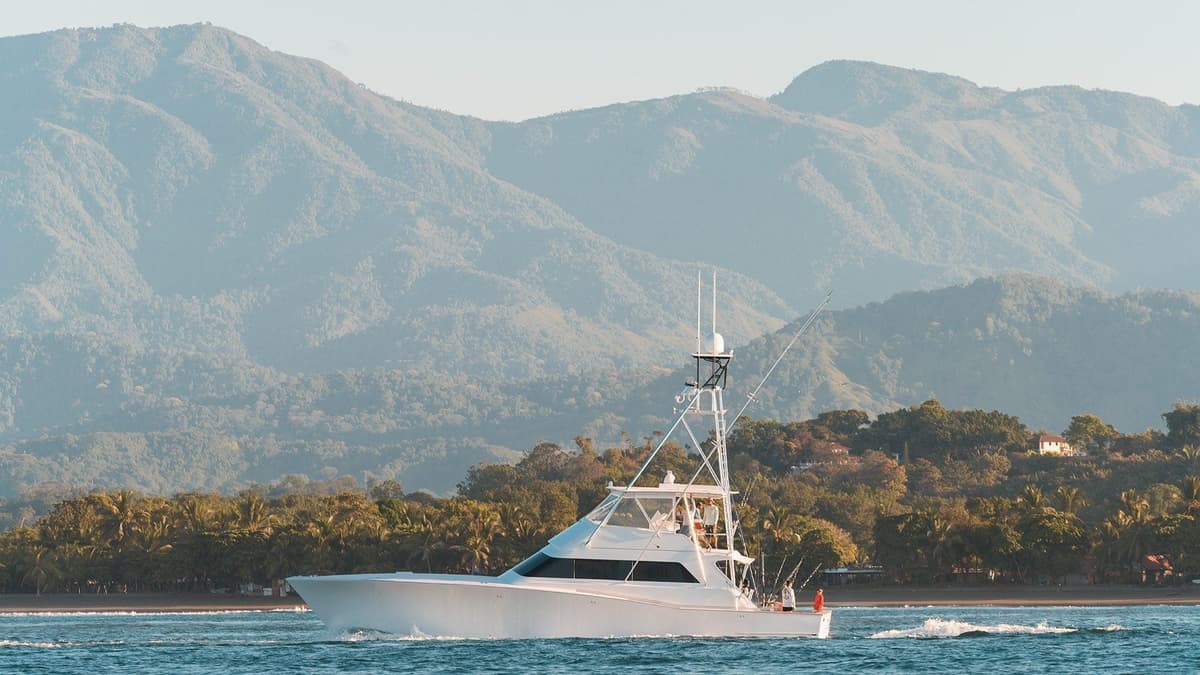 Sportfishing boat cruising on blue waters with lush green mountains in the background under a clear sky