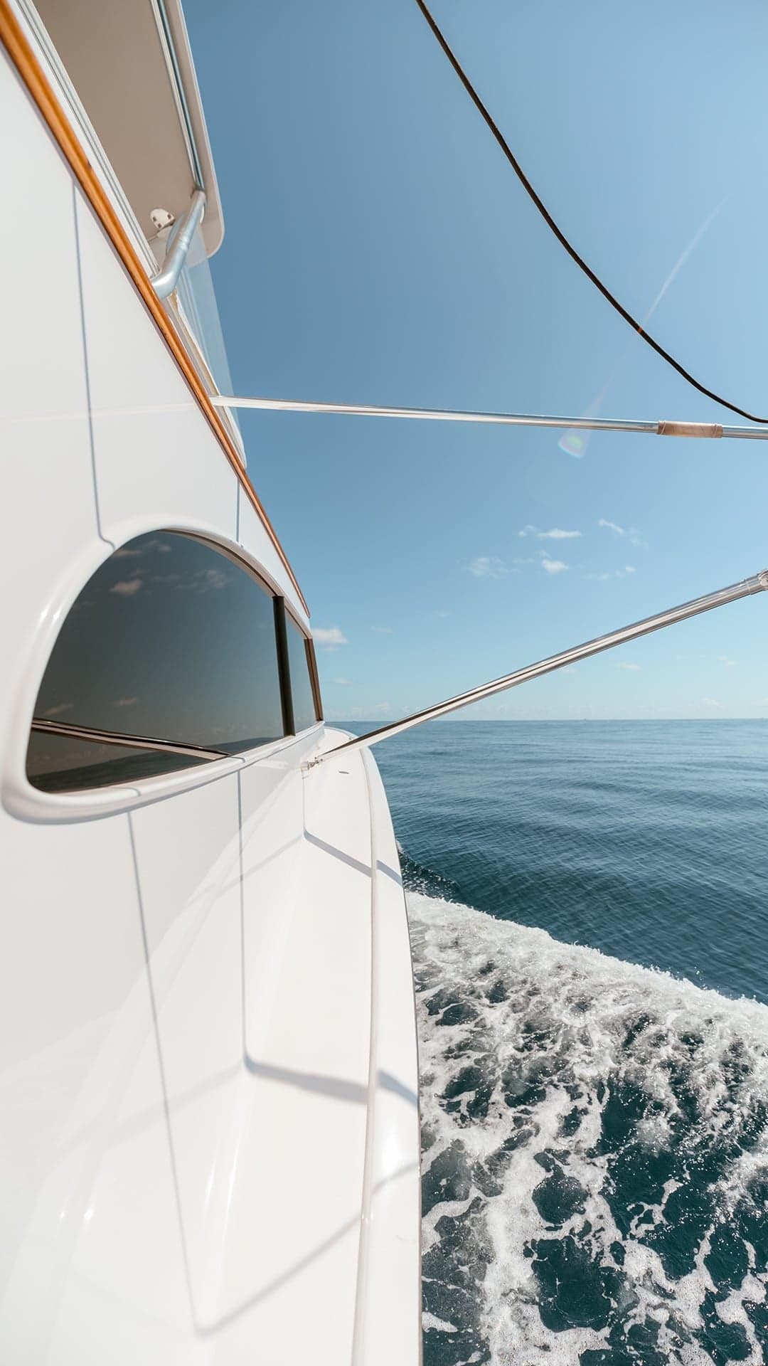 Side view of a luxurious yacht gliding through clear blue ocean waters, reflecting the bright sky