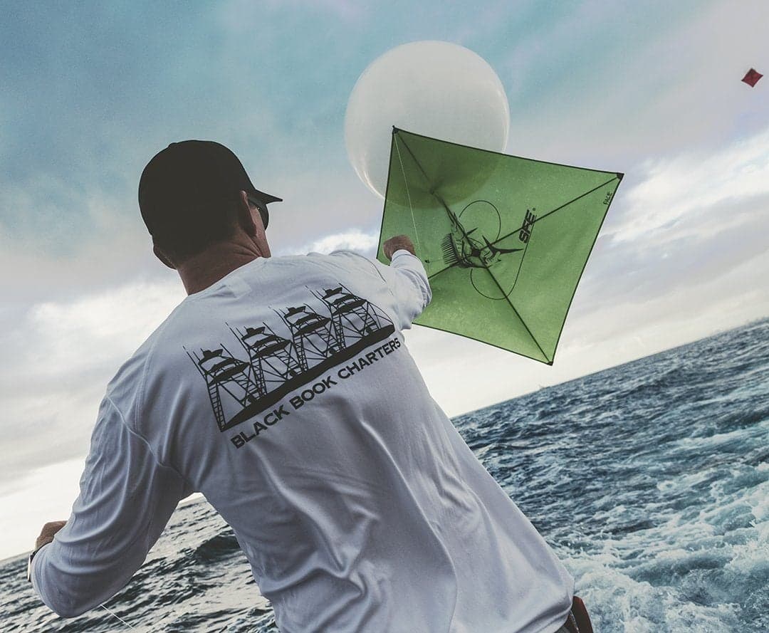 Person on a fishing boat deploying a green kite over the ocean