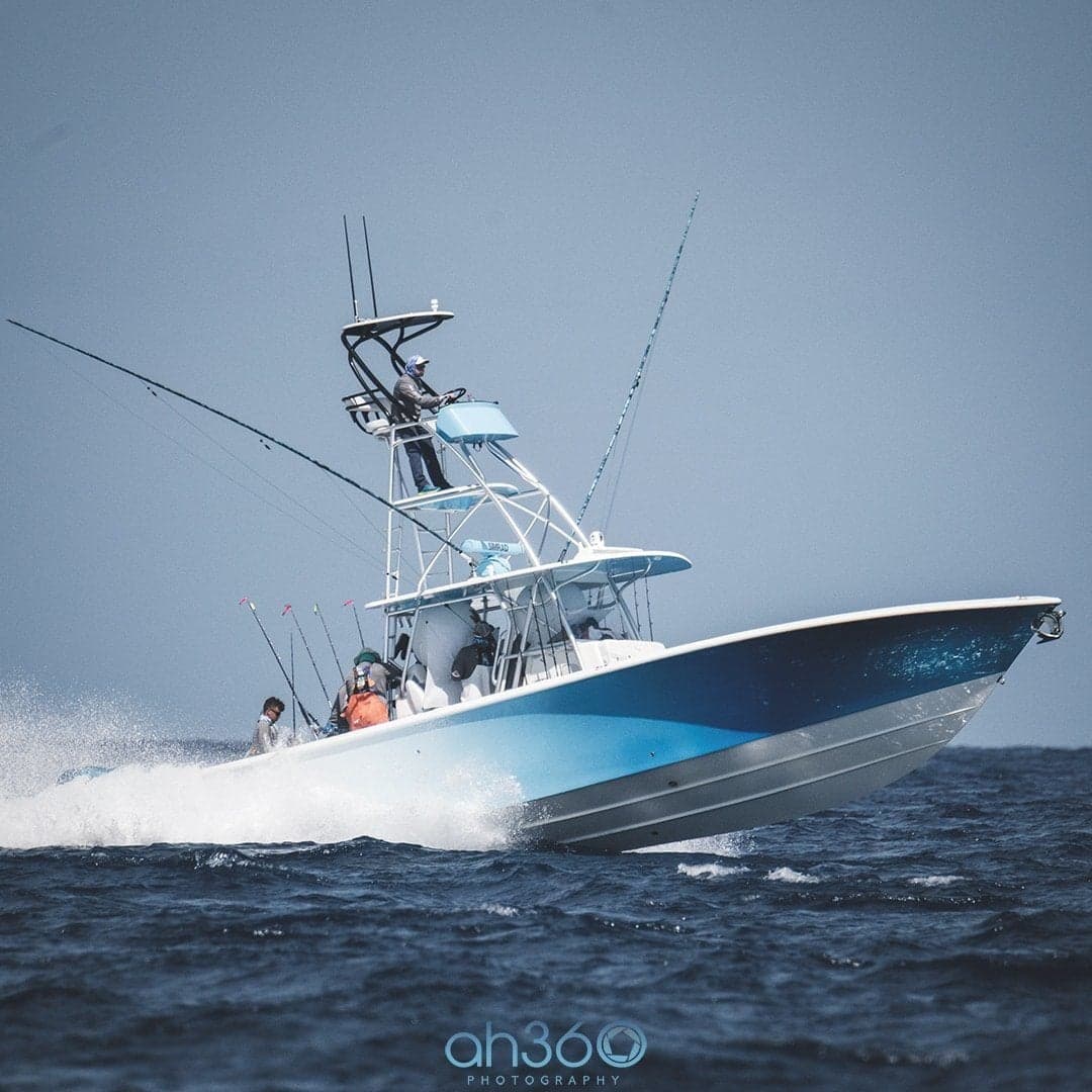 High-speed sportfishing boat navigating through waves with multiple fishing rods and a tower