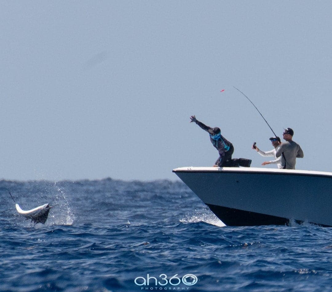 Three anglers on a boat capturing the moment of a fish leaping out of the water during deep-sea fishing