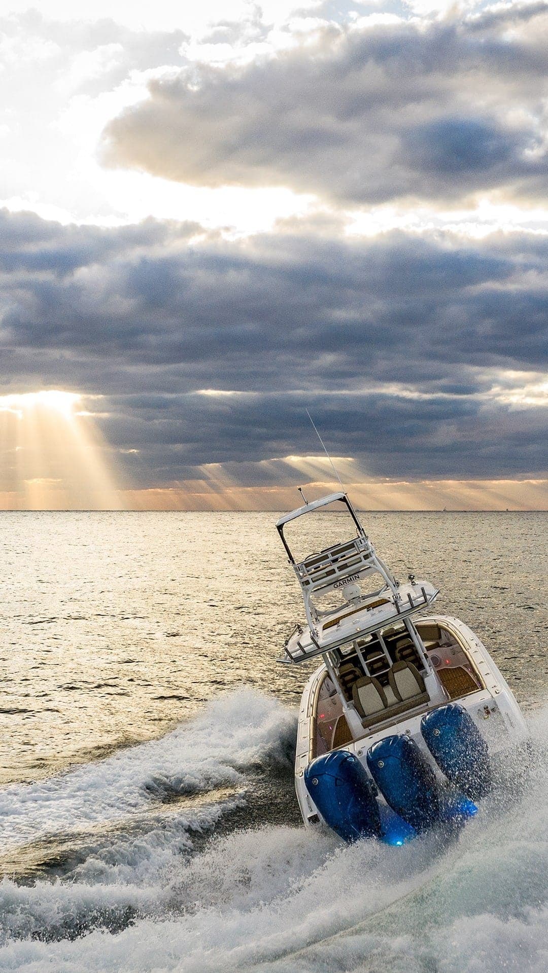 Sportfishing boat with four powerful outboard engines cutting through ocean waves under a dramatic sky