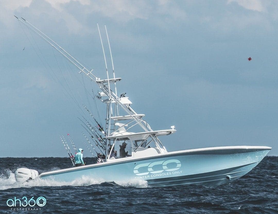 A sleek sportfishing boat navigating through the open ocean with multiple fishing rods and a vibrant blue hull