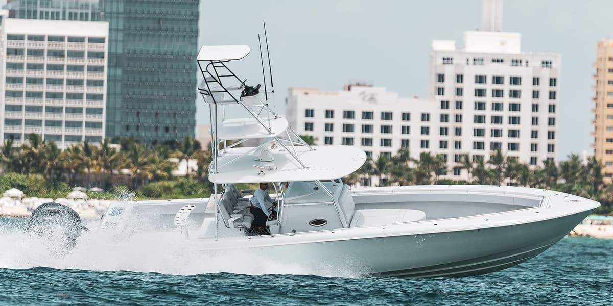 A large, white sportfishing boat cruising through blue waters with urban buildings and palm trees in the background