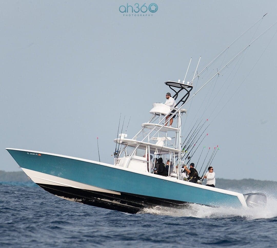 Sportfishing boat in full throttle with crew onboard, featuring multiple fishing rods and a deep blue hull