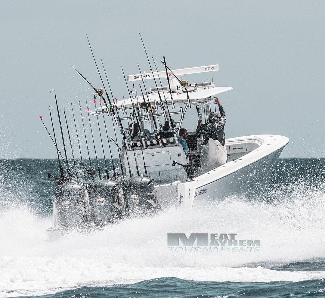 A powerful sportfishing boat cutting through the ocean waves with multiple fishing rods and outboard motors