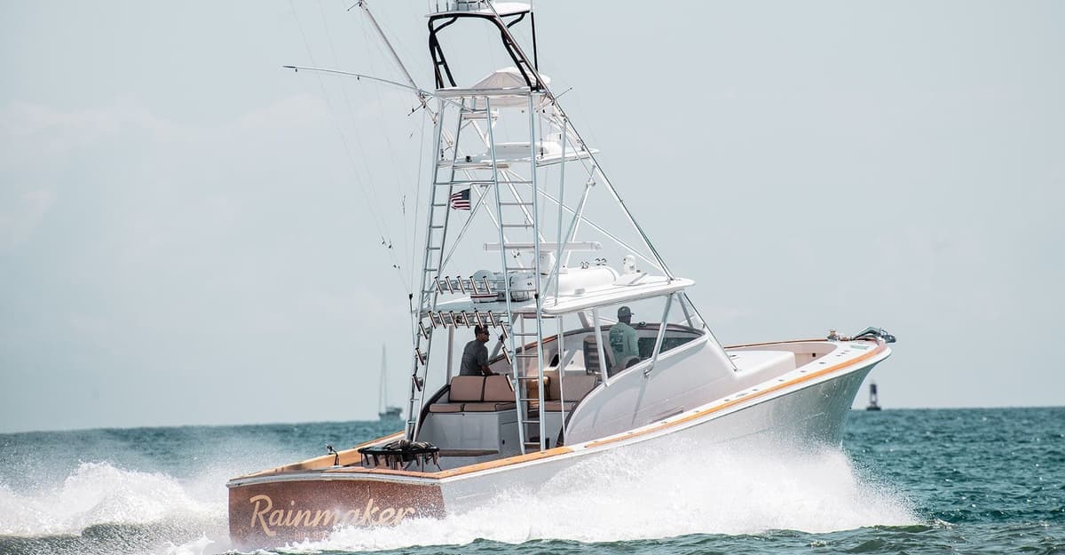 A sportfishing boat named Rainmaker gliding through ocean waves, featuring a tower with outriggers and crew on board
