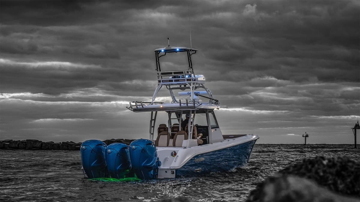 A modern sportfishing boat with three blue outboard motors navigating through dark and cloudy waters