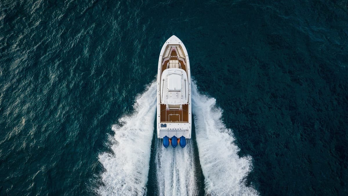 Aerial view of a luxurious yacht cruising through deep blue ocean waters, leaving white foamy trails