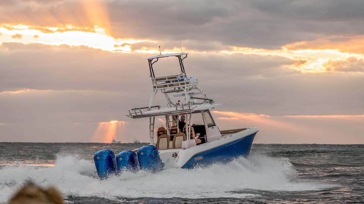 Sportfishing boat navigating through ocean waves with a dramatic sunset and cloudy sky backdrop