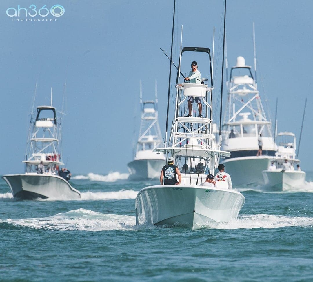 A fleet of sportfishing boats cruising in formation on open waters under a clear blue sky