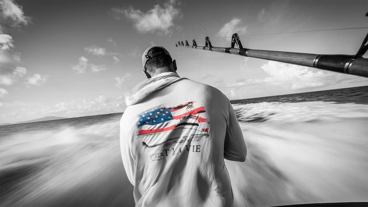 Angler in motion wearing a flag-themed shirt on a speeding boat, with a rod extended over the ocean