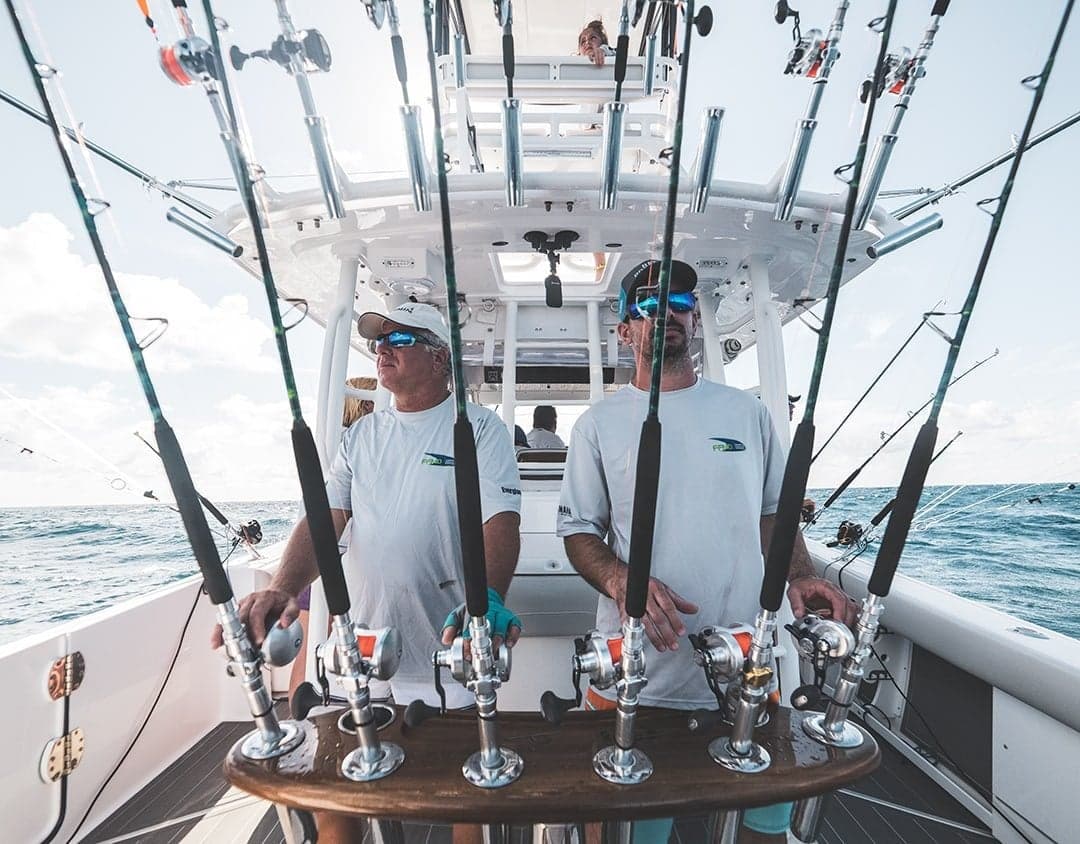 Two anglers on a sportfishing boat with multiple fishing rods navigating calm ocean waters