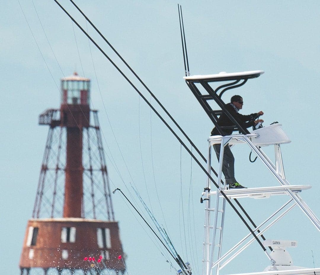 Angler at the helm on a sportfishing boat tower with fishing rods and a scenic lighthouse background