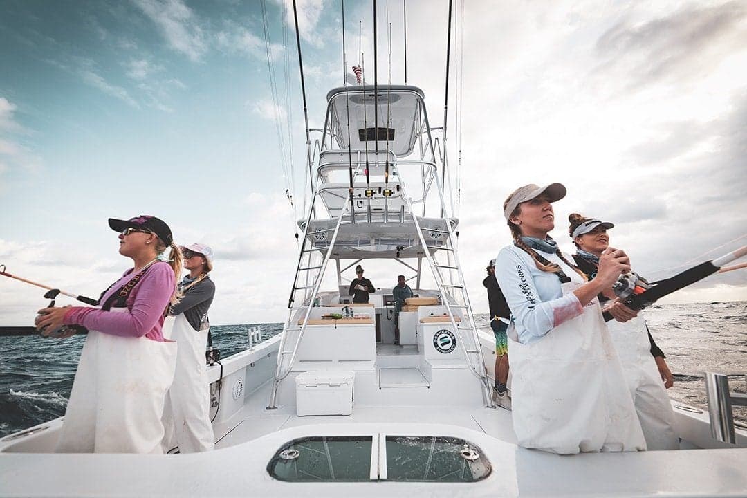 Group of anglers on a fishing boat actively engaged in sportfishing against open sea and cloudy sky