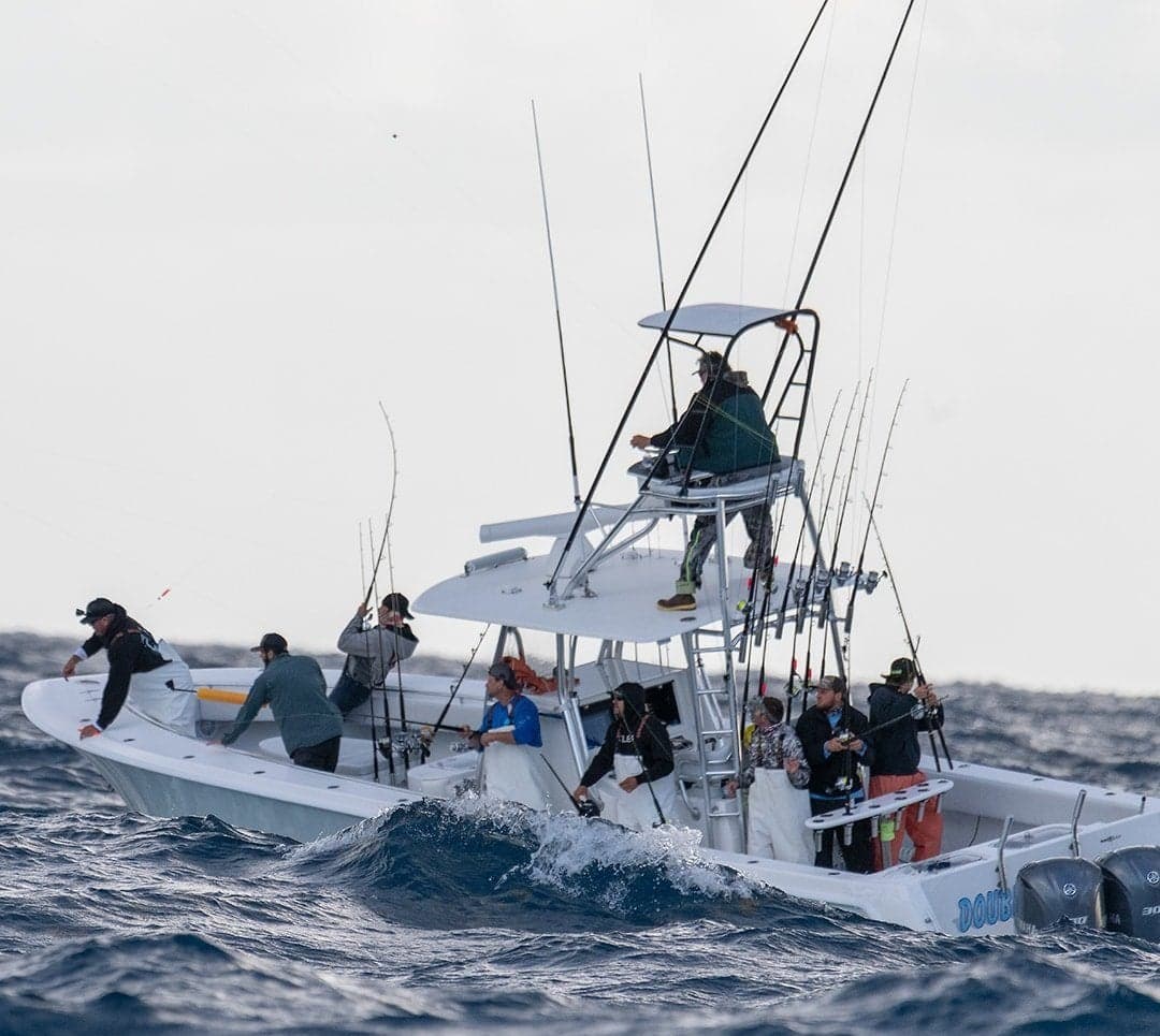 Group of anglers on a sportfishing boat navigating choppy waters with multiple fishing rods and a tower