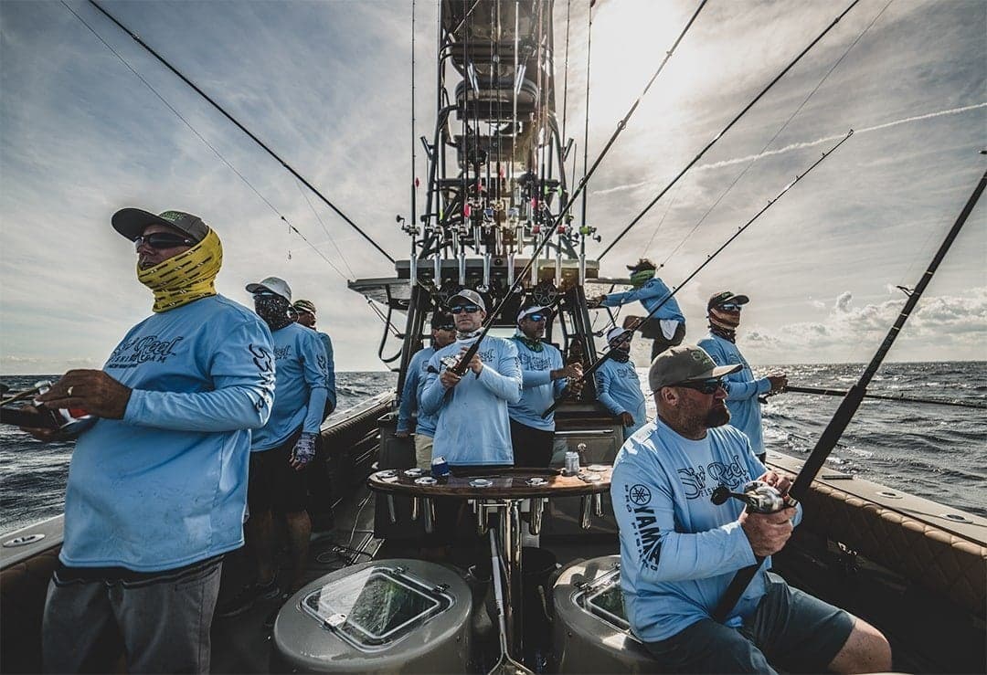 Group of anglers on a sportfishing boat in action, wearing matching blue shirts and caps