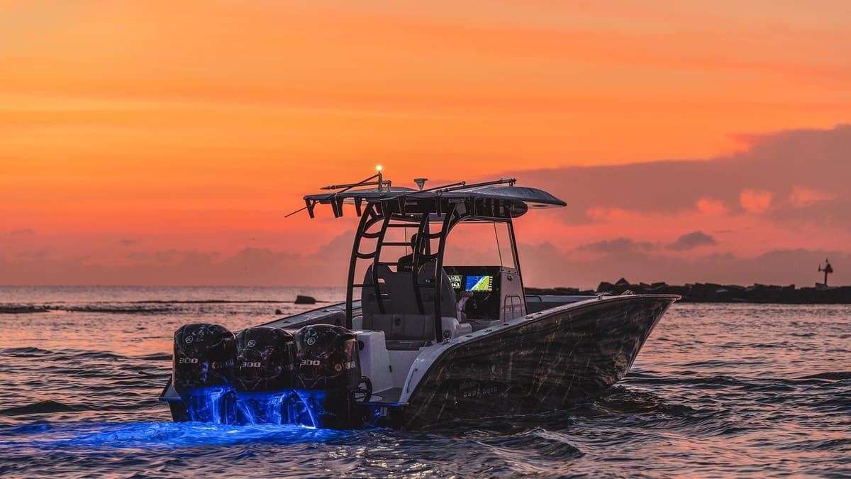 Sportfishing boat with triple engines and glowing blue underwater lights cruising at sunset