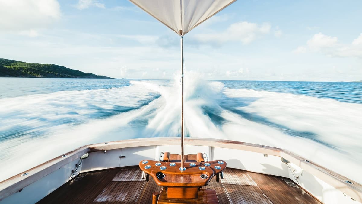 Sportfishing boat speeding across clear ocean waters, captured from the stern with a view of the wake and distant green hills