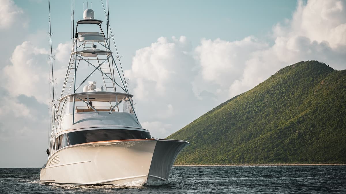 Front view of a luxury yacht navigating calm waters with a lush green hill in the background