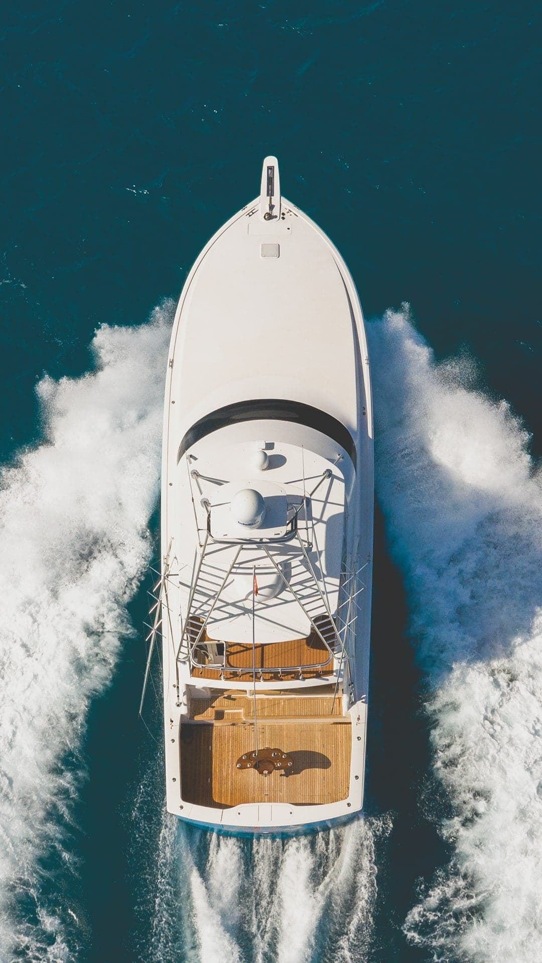 Aerial view of a sportfishing boat with a wooden deck, slicing through deep blue waters at high speed