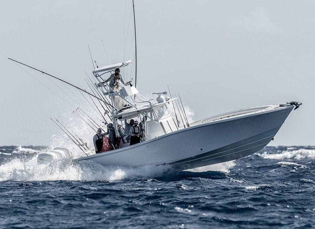 Sleek white sportfishing boat navigating choppy waves, equipped with multiple fishing rods and antennas