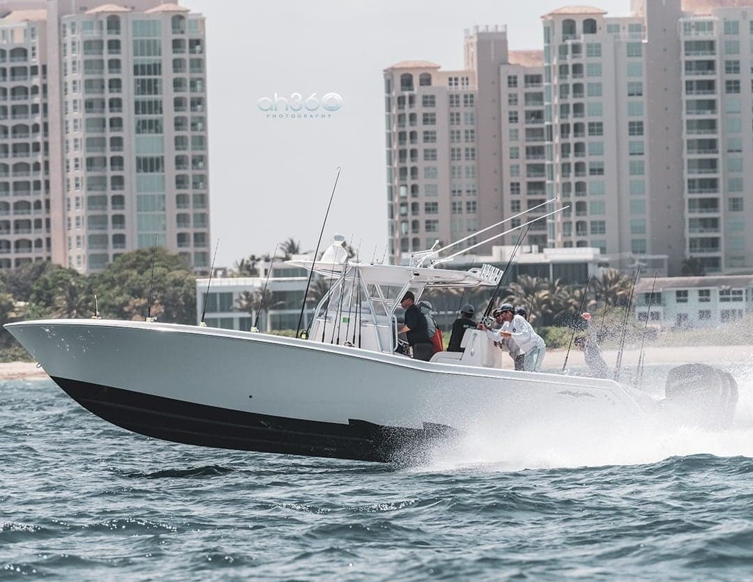 A dynamic sportfishing boat speeds across the water with high-rise buildings in the background