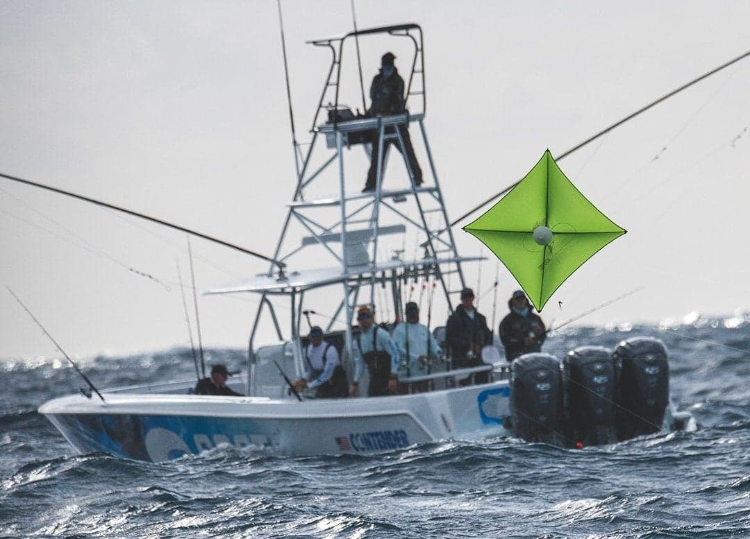 Sportfishing boat navigating through waves with anglers on deck and a green kite overhead