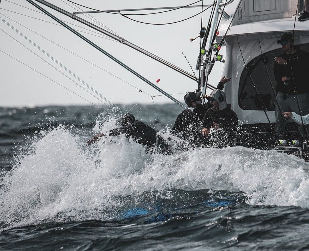 Anglers battling waves on a fishing boat equipped with multiple fishing rods during a sportfishing expedition