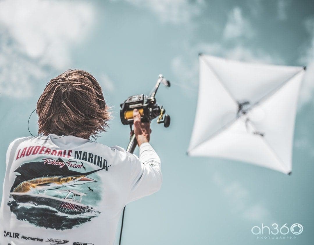 Angler with fishing reel and rod against a bright sky wearing a Lauderdale Marina Fishing Team shirt