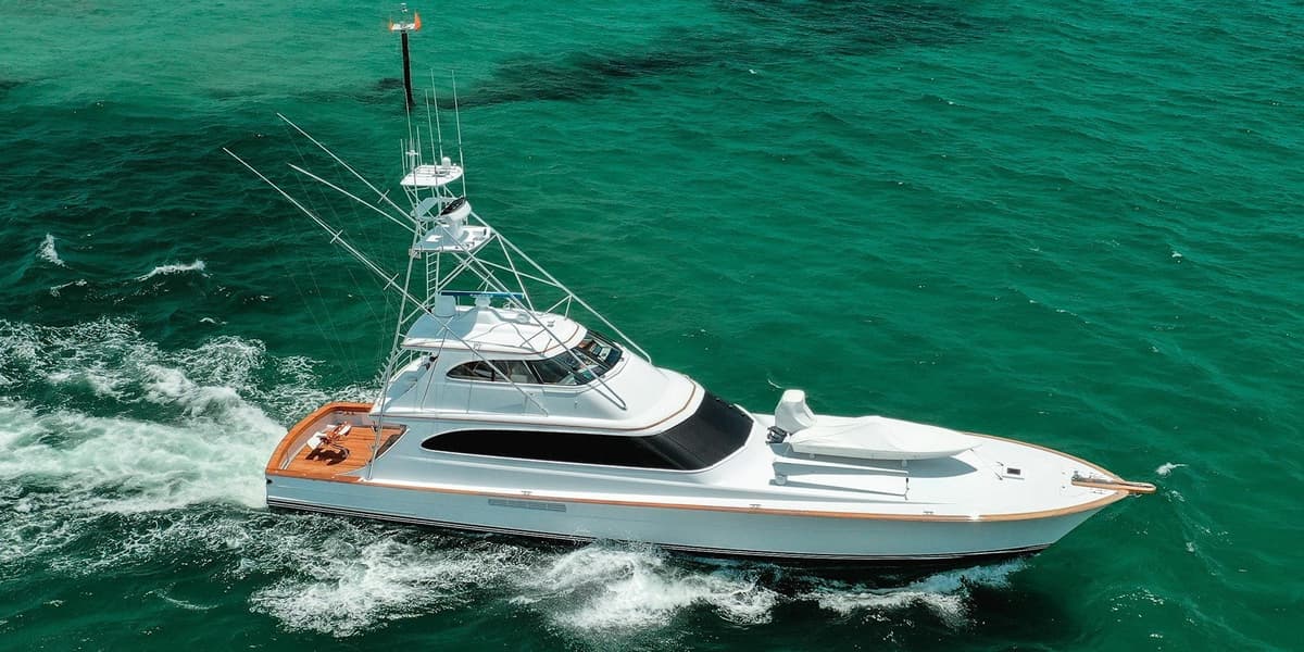 A sleek, white sportfishing yacht cruising through vibrant turquoise waters with multiple rod holders and an upper helm