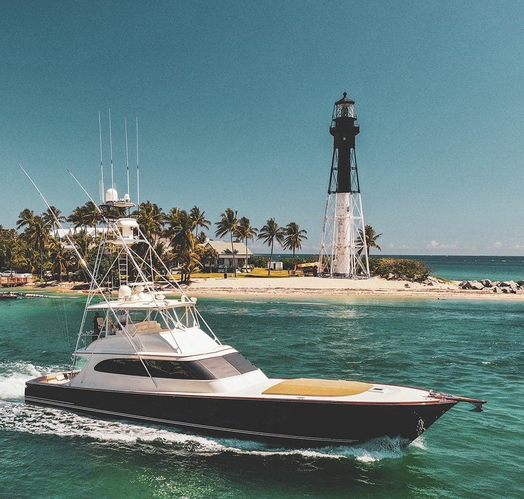 Elegant sportfishing boat cruising near a picturesque lighthouse, surrounded by palm trees and turquoise waters