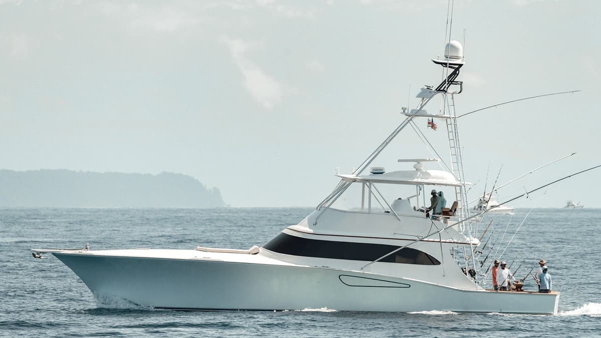 Side view of a sleek, modern sportfishing yacht cruising on open waters with several people onboard and multiple fishing rods