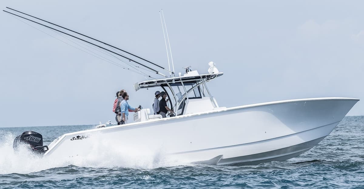 A powerful white sportfishing boat speeding through open waters, equipped with multiple fishing rods and an outboard engine