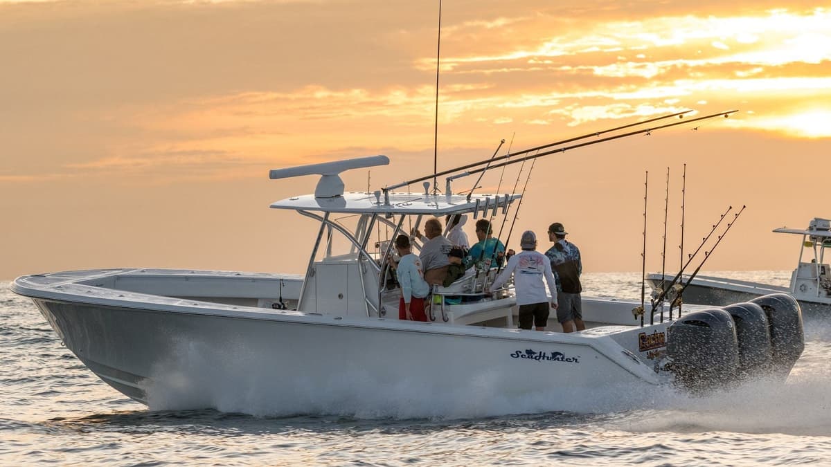 A group of anglers on a white sportfishing boat navigating the ocean at sunset with multiple fishing rods ready