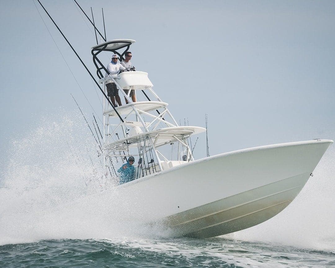Dynamic photo of a sportfishing boat cutting through rough seas with three people on board