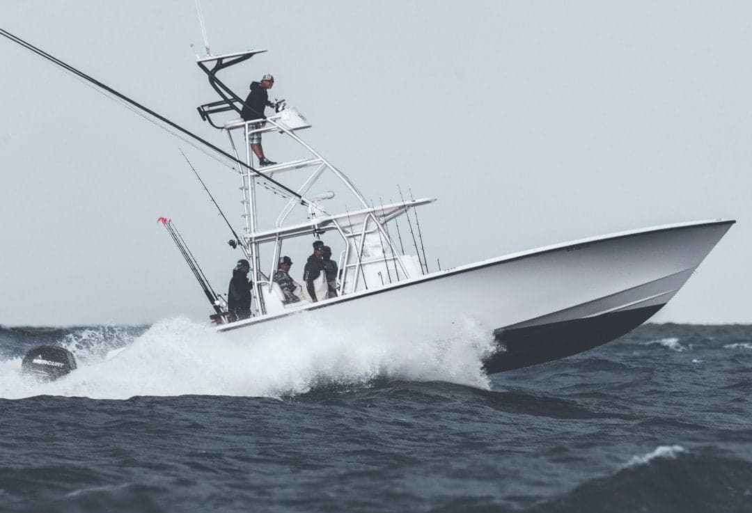 A sleek, white sportfishing boat cutting through choppy waves with several people aboard
