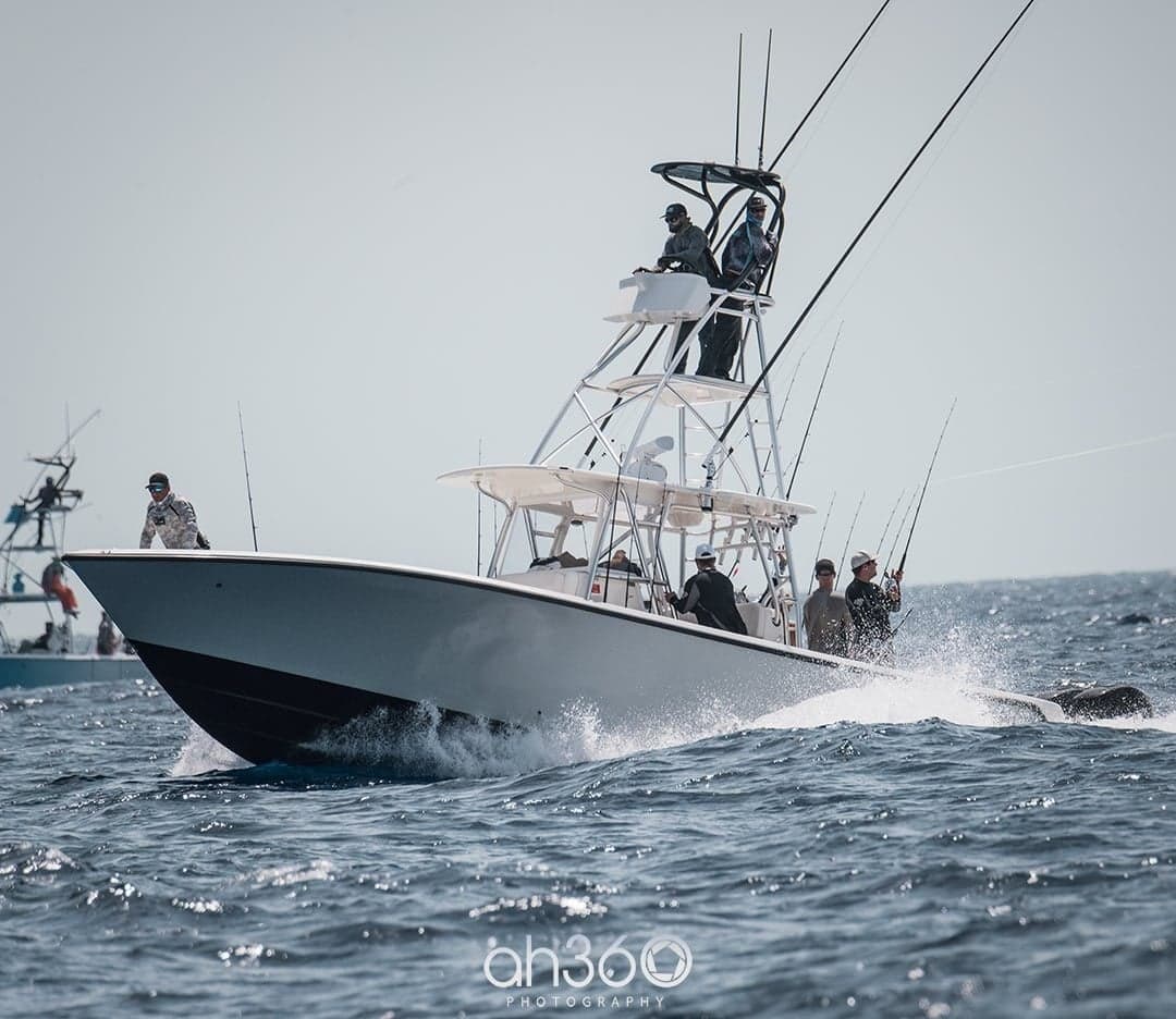 Sportfishing boat navigating through waves with anglers on deck during a sunny day on the ocean
