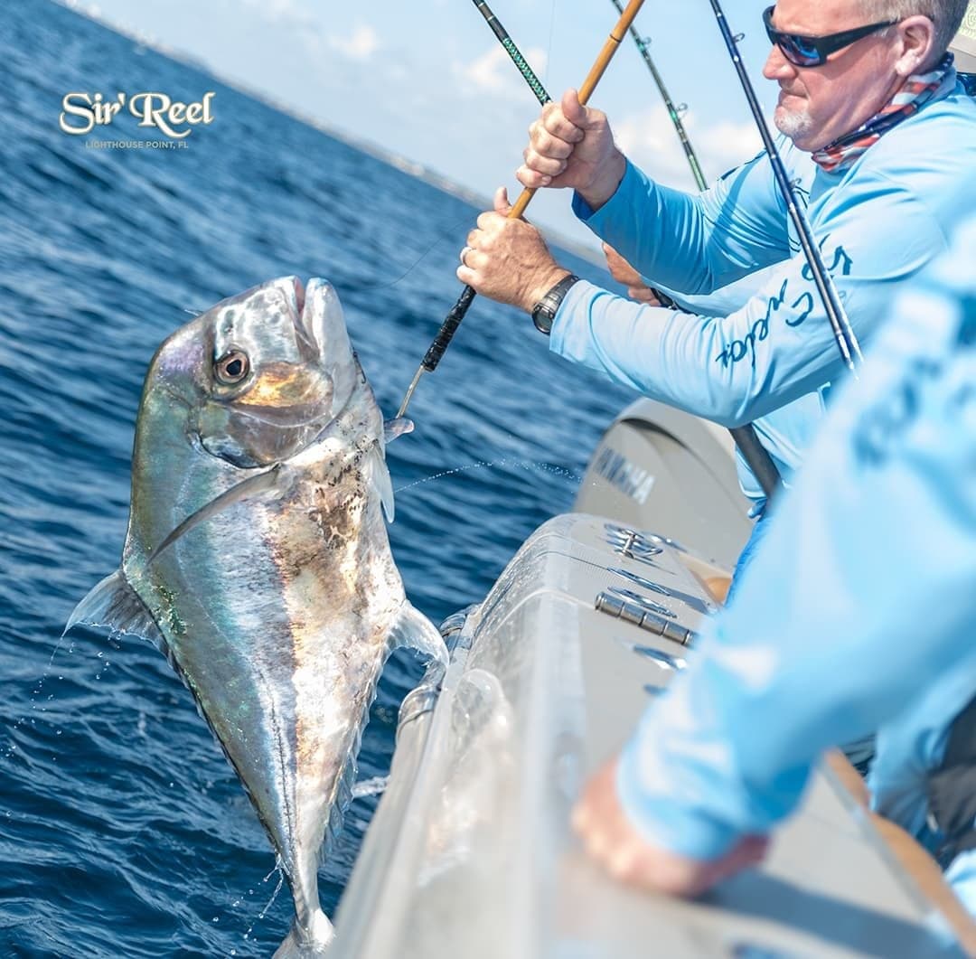 Fishermen in blue shirts bringing a large fish on board a sportfishing boat in a blue ocean setting