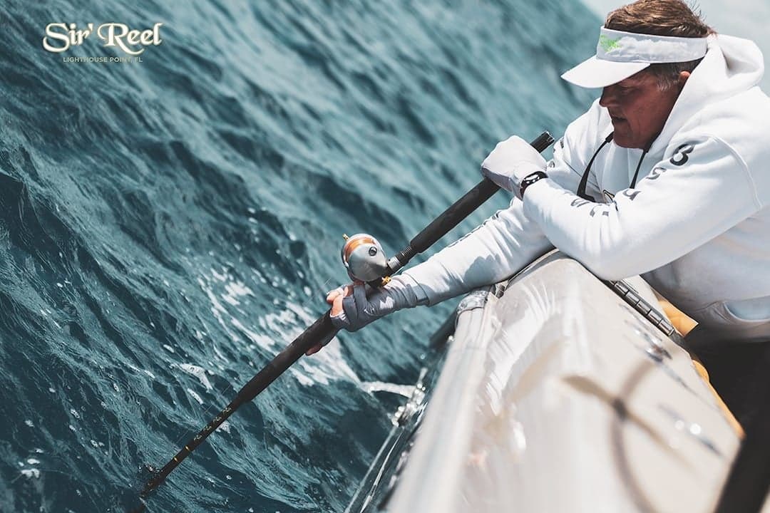 Close-up of an angler reeling in a catch over the side of a boat with ocean waves in the background