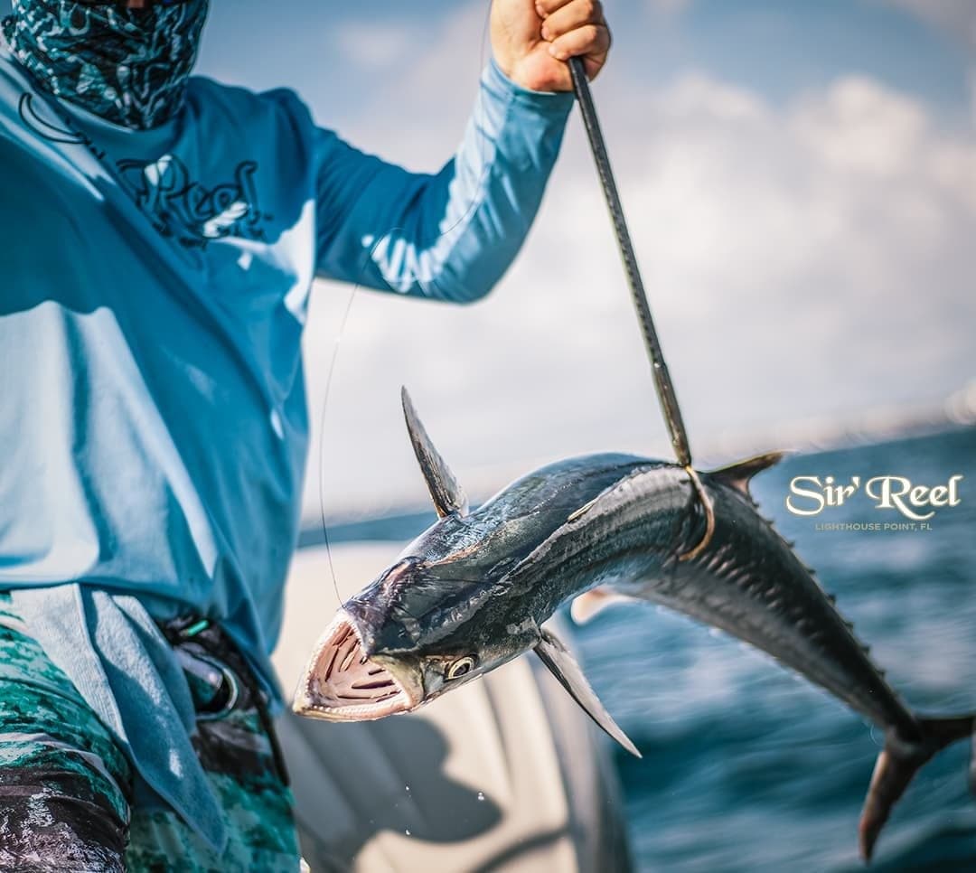 Angler holding a freshly caught sports fish on a boat, wearing blue fishing apparel with an ocean backdrop