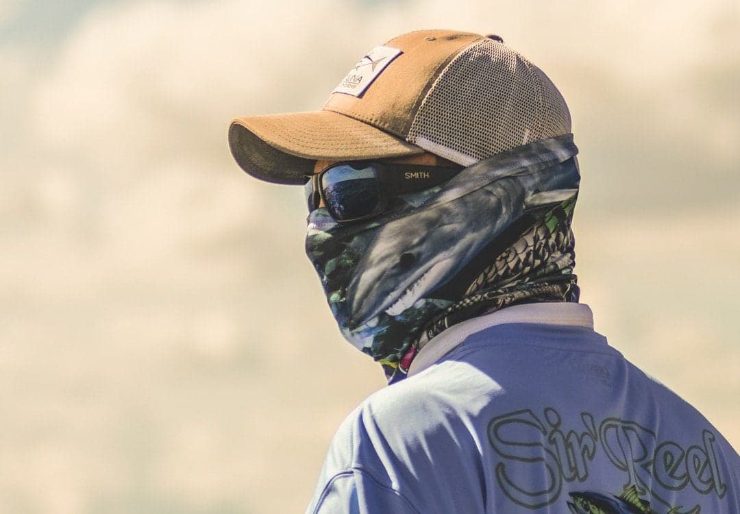 Angler in protective gear and branded shirt looks out over the water with polarized sunglasses