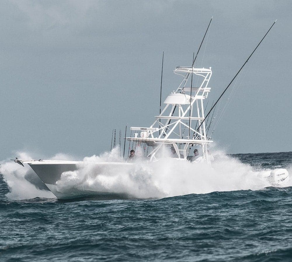 Sportfishing boat powering through ocean waves with fishing rods and outriggers visible