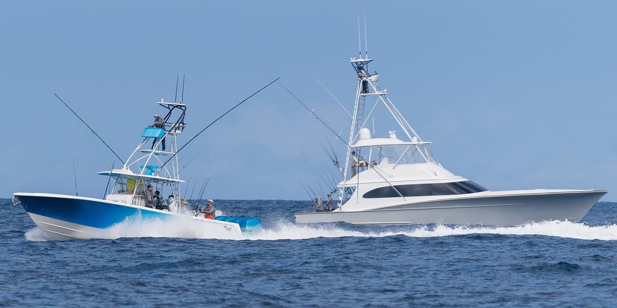 Two sporty fishing boats with multiple fishing rods cruise on the open sea, cutting through waves under a clear blue sky