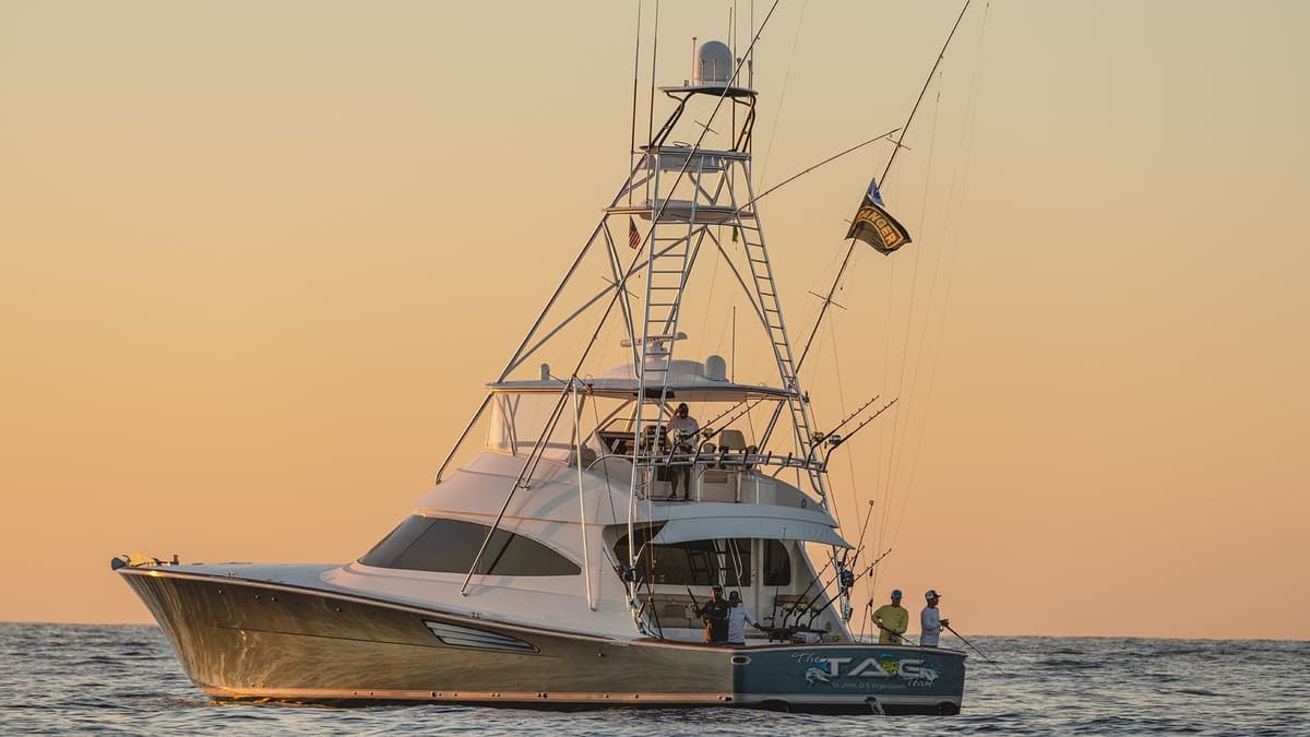 Sportfishing boat cruising on calm waters at sunset with an orange sky and a group of anglers on deck
