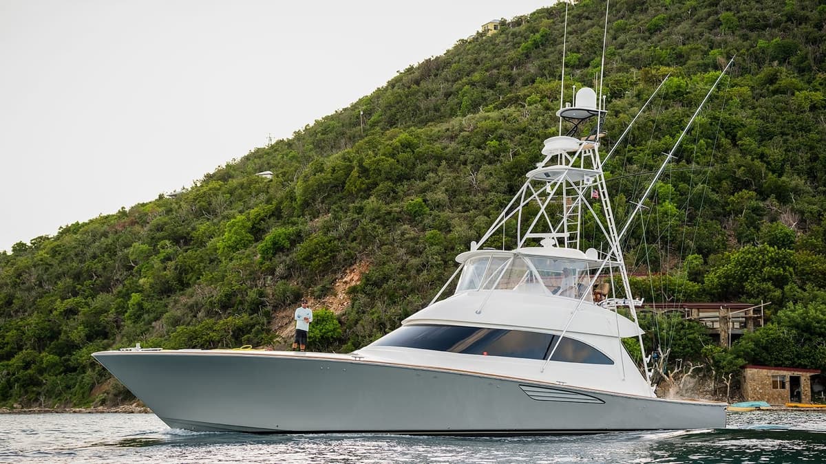 A sleek sportfishing yacht anchored near a lush hillside, featuring tall fishing rods and modern navigation equipment