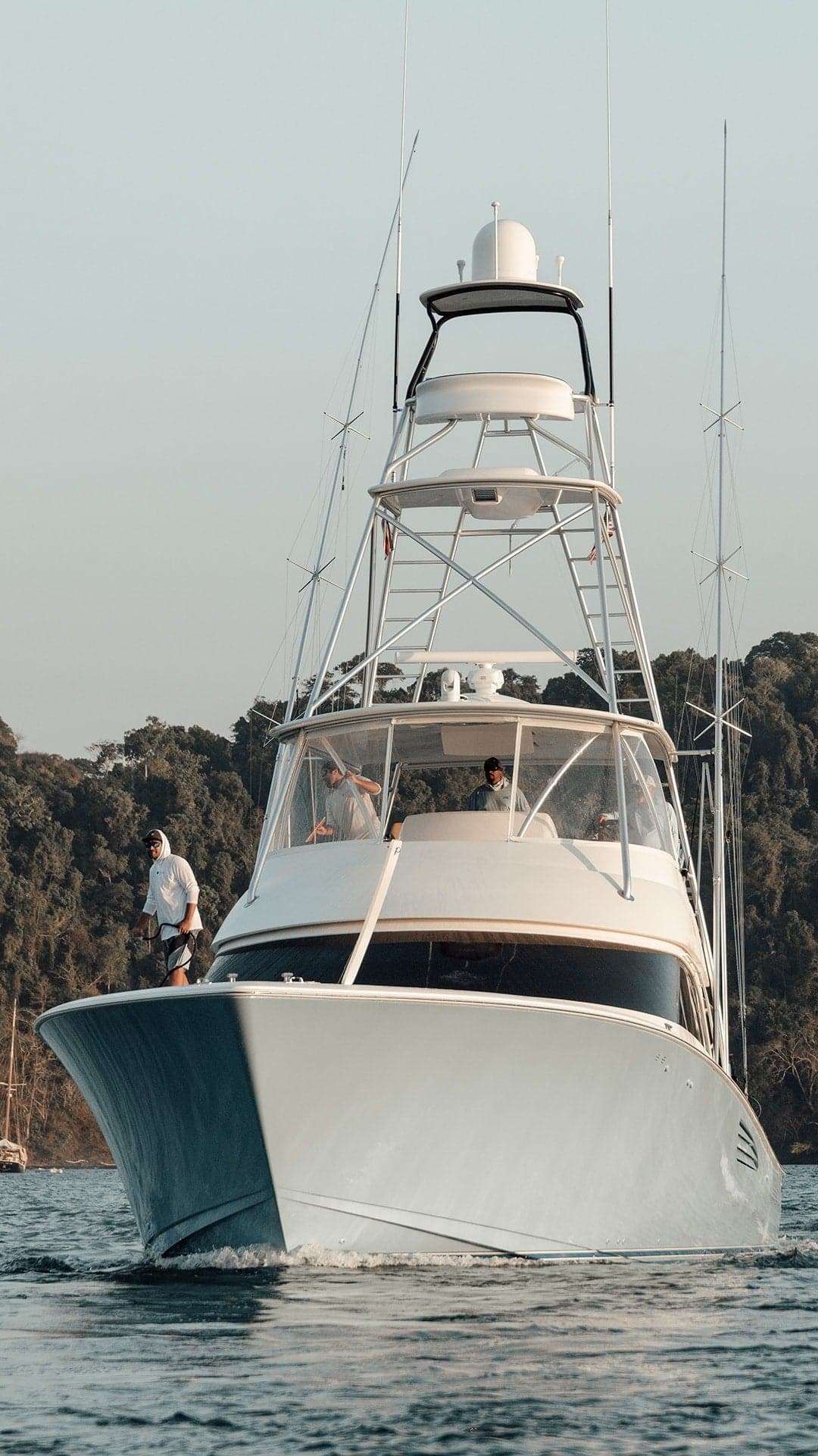 A sportfishing yacht with a high tower, featuring three people and an American flag