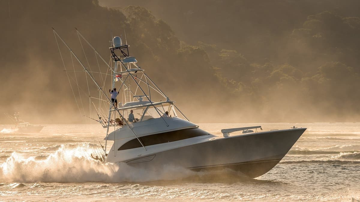 A sleek sportfishing boat navigating through misty waters at sunrise with anglers seen onboard amidst towering fishing rods